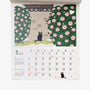 Tabineko Wandkalender 2027 mit einer schwarzen Katze vor einer Mauer mit blühenden rosa Kamelien im März-Kalenderblatt.